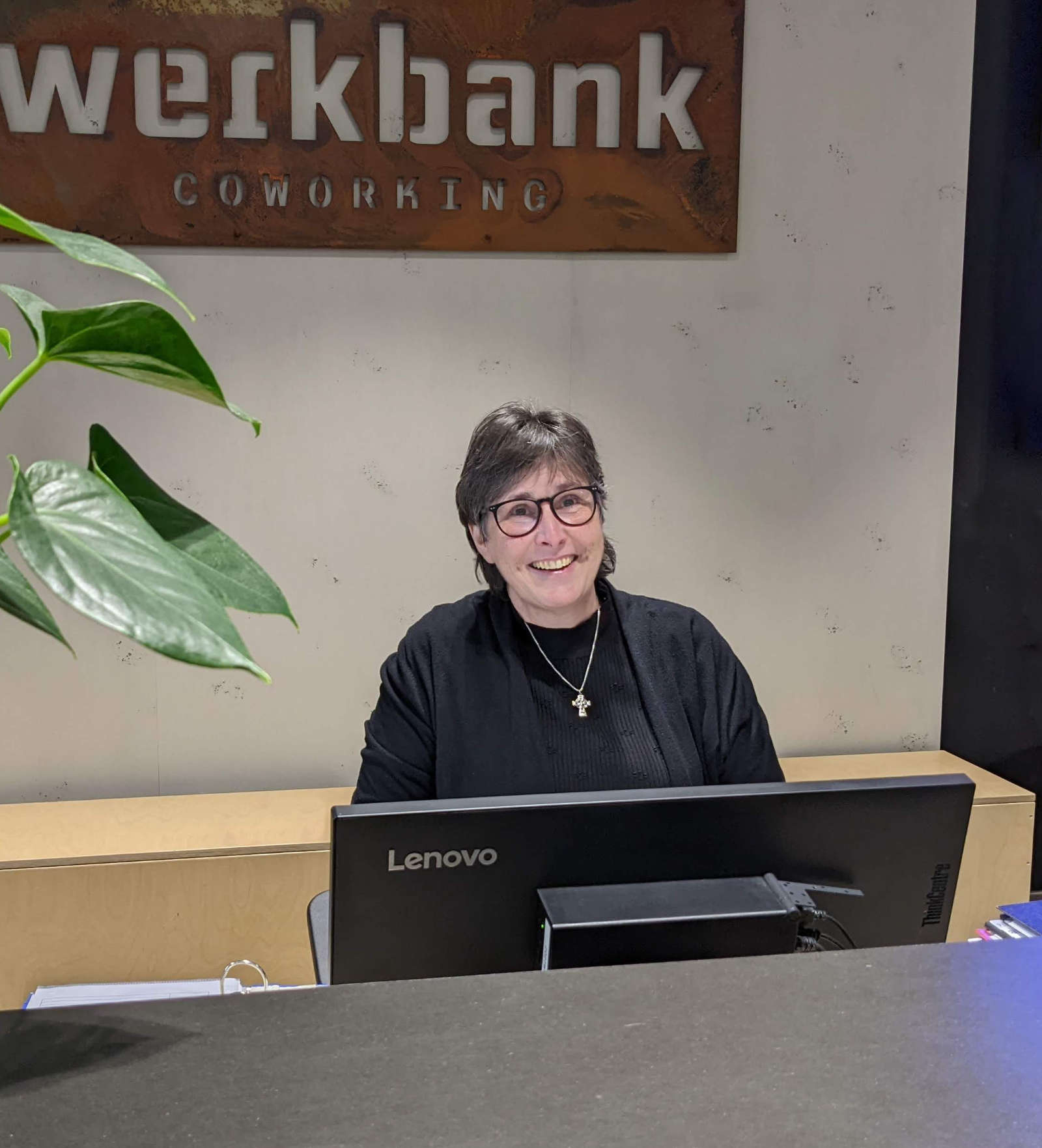 Claudia Plum am Empfangsschreibtisch in der Werkbank. Im Hintergrund das Werkbank-Logo ausgestanzt aus einer großen Metallplatte